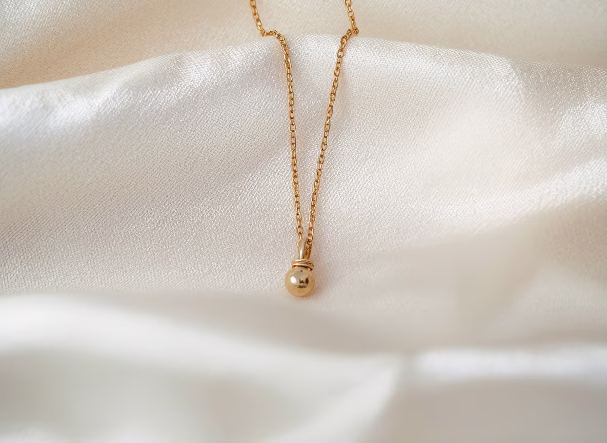 Fine gold chain necklace with a small pendant resting on cream silk